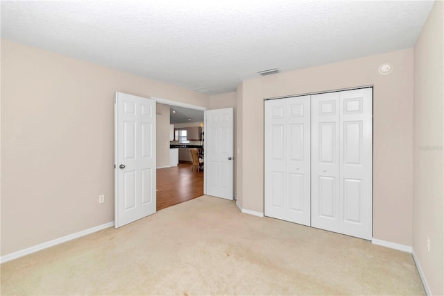 unfurnished bedroom with a textured ceiling, light carpet, and a closet