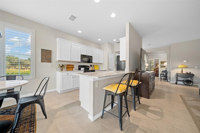 kitchen with light stone counters, black appliances, white cabinetry, a breakfast bar area, and light tile patterned flooring