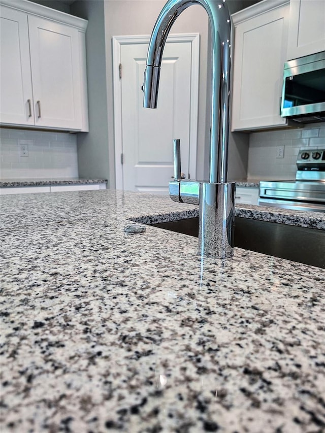 kitchen with tasteful backsplash, white cabinetry, light stone counters, and appliances with stainless steel finishes