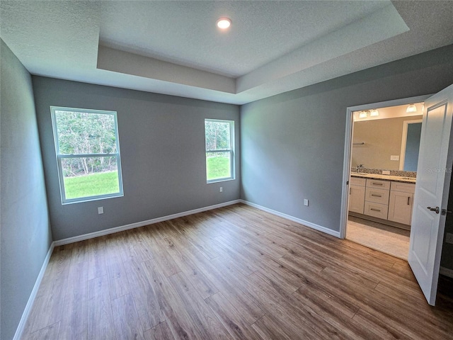 unfurnished bedroom with a raised ceiling, ensuite bathroom, light hardwood / wood-style flooring, and a textured ceiling