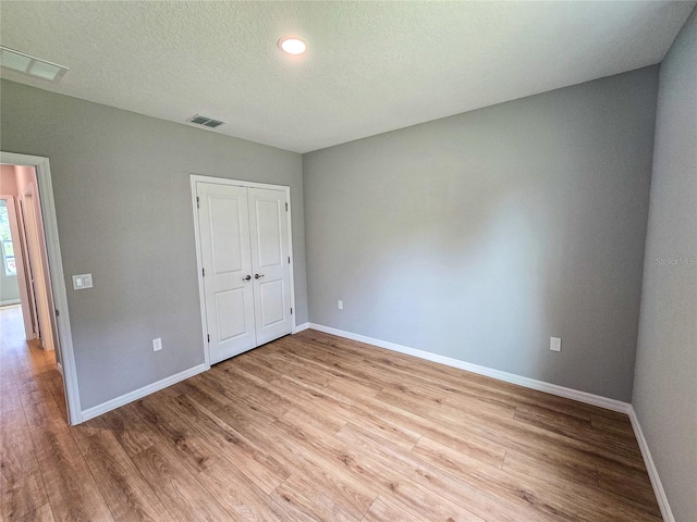 unfurnished bedroom with a closet, a textured ceiling, and light hardwood / wood-style flooring