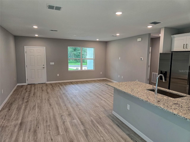 kitchen featuring white cabinetry, sink, light stone counters, stainless steel fridge, and light hardwood / wood-style floors