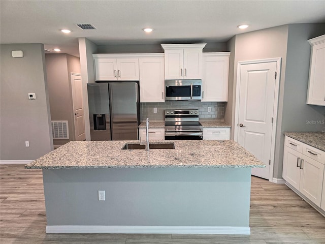 kitchen featuring light wood-type flooring, stainless steel appliances, sink, white cabinetry, and an island with sink