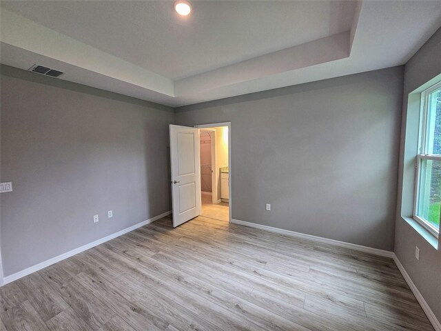 unfurnished bedroom with a tray ceiling and light wood-type flooring