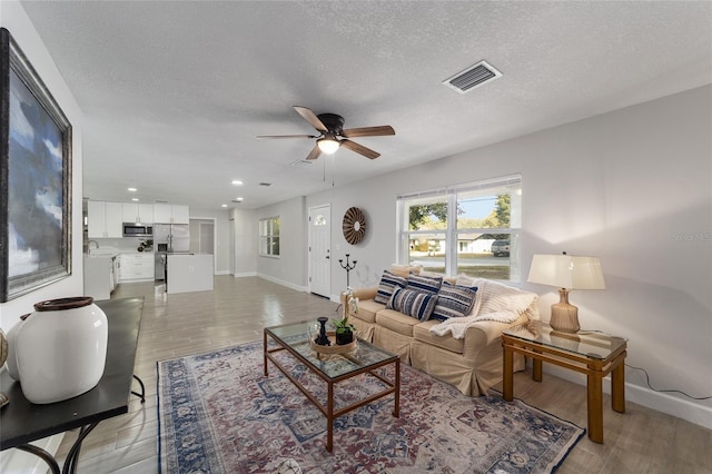 living room featuring ceiling fan, light hardwood / wood-style flooring, and a textured ceiling