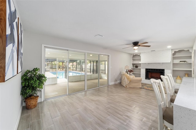 living room featuring ceiling fan, light hardwood / wood-style flooring, built in features, and a brick fireplace