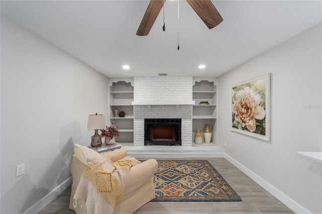 living room featuring a fireplace, built in shelves, hardwood / wood-style flooring, and ceiling fan