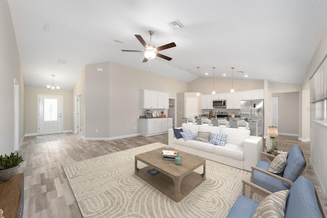 living room with ceiling fan with notable chandelier, light hardwood / wood-style floors, and lofted ceiling