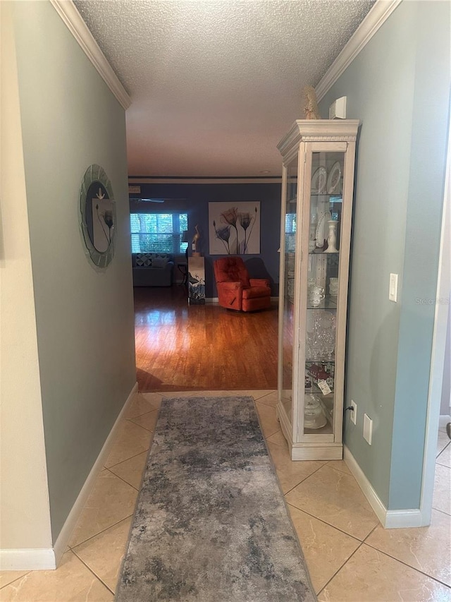 hallway with ornamental molding, a textured ceiling, and light wood-type flooring