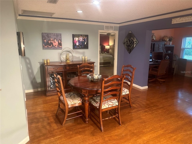 dining space with wood-type flooring, a textured ceiling, and ornamental molding