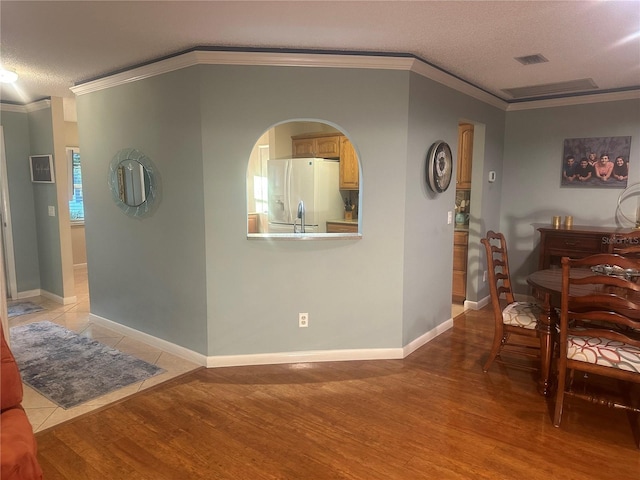 dining space featuring crown molding, light hardwood / wood-style flooring, and a textured ceiling