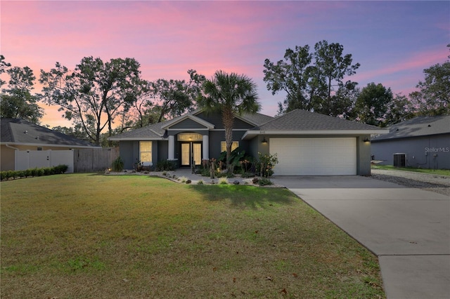 view of front of property featuring a lawn, central air condition unit, and a garage