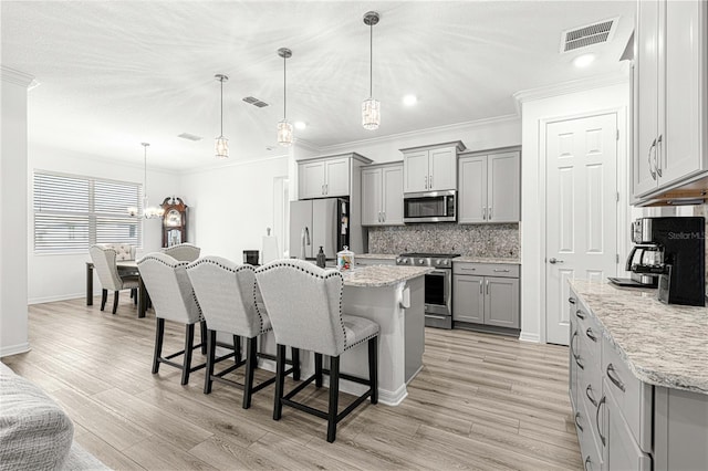 kitchen featuring a kitchen island with sink, stainless steel appliances, decorative light fixtures, and light wood-type flooring