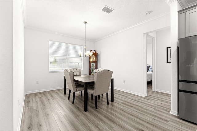 dining room featuring crown molding, light hardwood / wood-style flooring, a textured ceiling, and an inviting chandelier