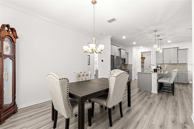 dining space with ornamental molding, light hardwood / wood-style flooring, a notable chandelier, and sink