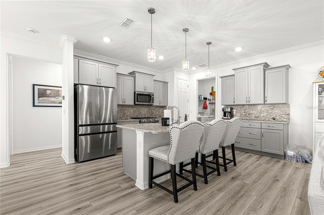 kitchen featuring stainless steel appliances, light hardwood / wood-style flooring, an island with sink, pendant lighting, and a kitchen bar