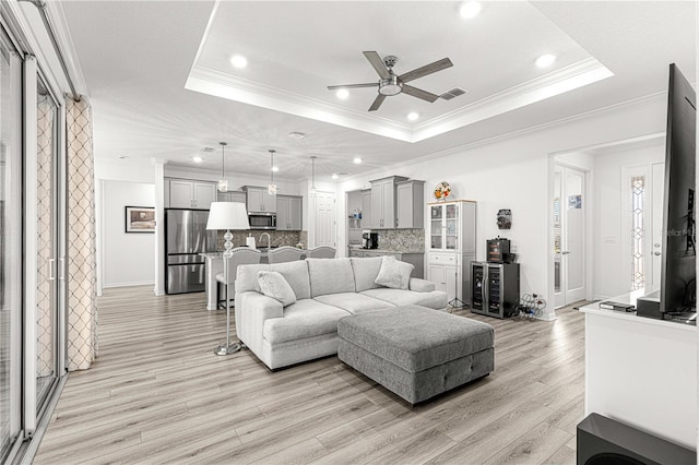 living room featuring ceiling fan, a raised ceiling, crown molding, and light hardwood / wood-style flooring