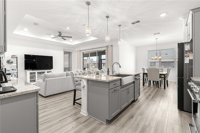 kitchen featuring ceiling fan with notable chandelier, sink, decorative light fixtures, a center island with sink, and gray cabinets