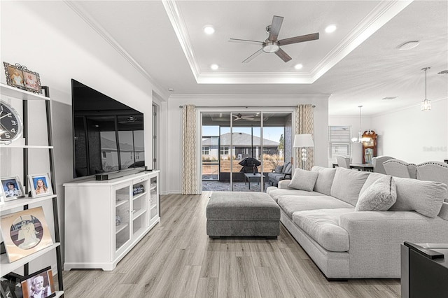 living room with ceiling fan with notable chandelier, light hardwood / wood-style floors, a raised ceiling, and ornamental molding