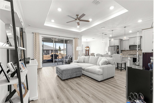 living room with a raised ceiling, ceiling fan, light hardwood / wood-style floors, and ornamental molding