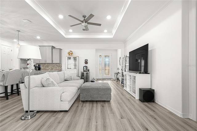 living room with a raised ceiling, light hardwood / wood-style flooring, ceiling fan, and ornamental molding