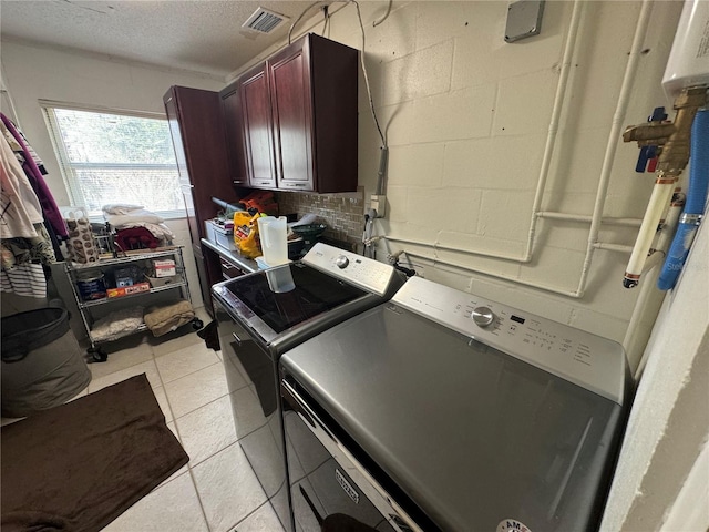 laundry room with washer and clothes dryer, cabinets, light tile patterned floors, and a textured ceiling