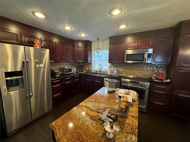 kitchen with sink, hanging light fixtures, dark stone countertops, a textured ceiling, and stainless steel appliances