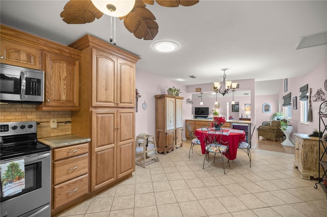 kitchen with decorative backsplash, ceiling fan with notable chandelier, stainless steel appliances, pendant lighting, and light tile patterned floors