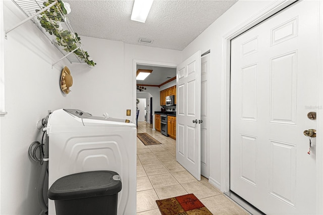 clothes washing area with independent washer and dryer, a textured ceiling, and light tile patterned floors