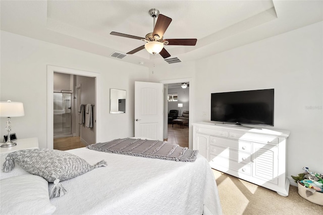 bedroom featuring carpet flooring, ensuite bathroom, ceiling fan, and a tray ceiling