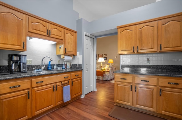 kitchen featuring wood-type flooring, backsplash, dark stone counters, and sink