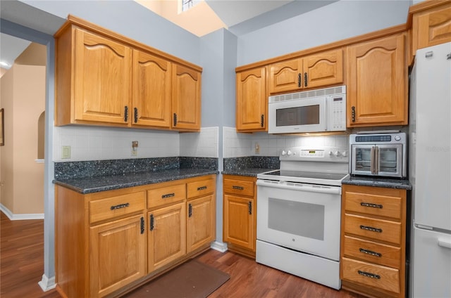 kitchen featuring backsplash, dark stone counters, white appliances, and hardwood / wood-style flooring