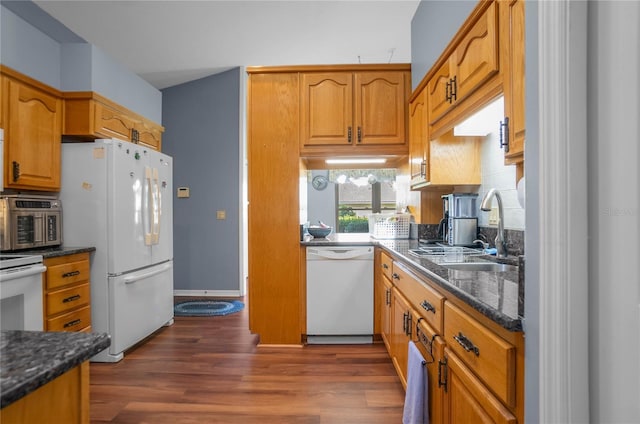 kitchen featuring dark stone countertops, white appliances, dark wood-type flooring, and sink