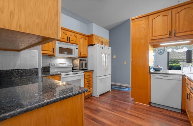 kitchen featuring wood-type flooring, white appliances, backsplash, and dark stone countertops