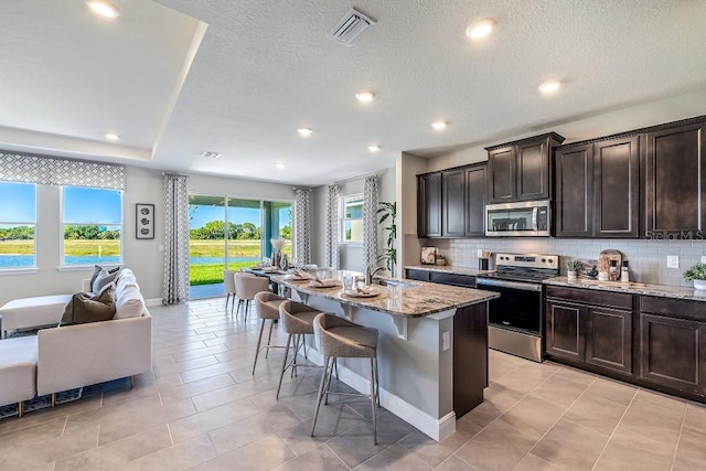 kitchen with a breakfast bar, a kitchen island with sink, appliances with stainless steel finishes, and tasteful backsplash