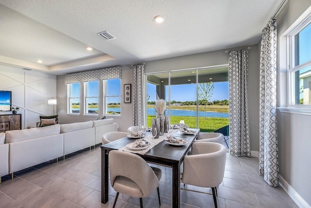 tiled dining room featuring a textured ceiling, a water view, plenty of natural light, and a tray ceiling