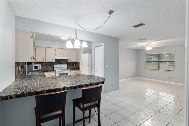 kitchen featuring kitchen peninsula, decorative backsplash, white appliances, ceiling fan with notable chandelier, and hanging light fixtures