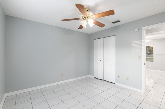 unfurnished bedroom featuring ceiling fan, light tile patterned floors, a textured ceiling, and a closet