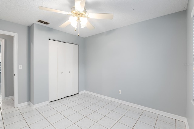 unfurnished bedroom featuring ceiling fan, light tile patterned floors, a textured ceiling, and a closet