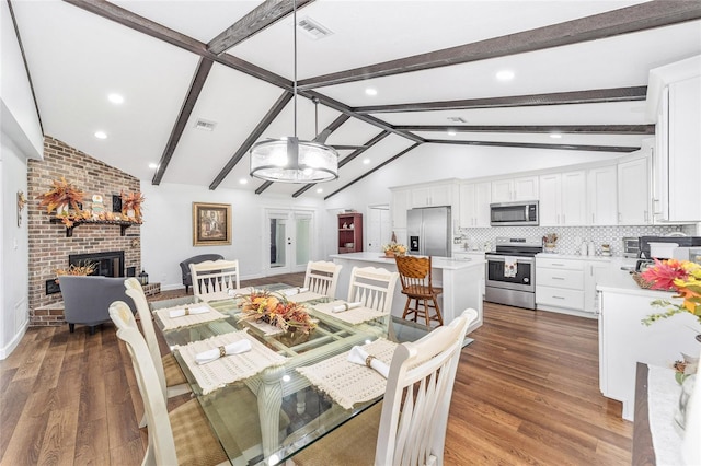 dining space featuring vaulted ceiling with beams, a brick fireplace, and dark wood-type flooring