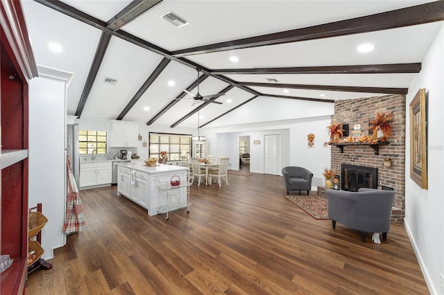 living room with vaulted ceiling with beams, ceiling fan, dark hardwood / wood-style flooring, and a brick fireplace