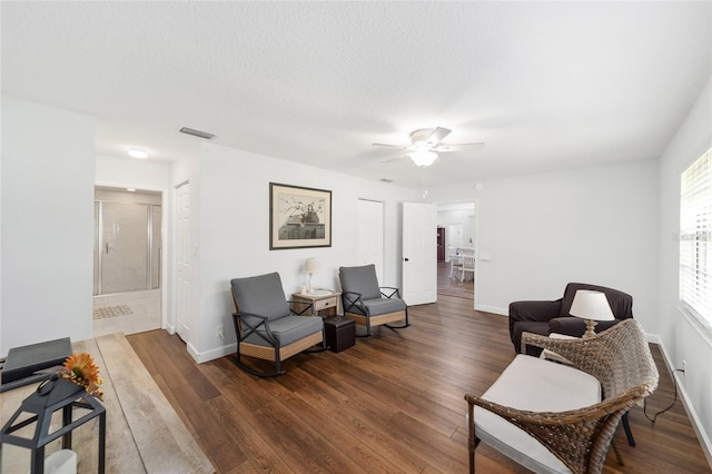 living area with ceiling fan, dark hardwood / wood-style flooring, and a textured ceiling