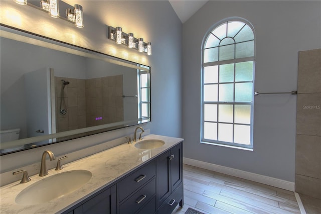 bathroom featuring hardwood / wood-style floors, vanity, vaulted ceiling, toilet, and a tile shower