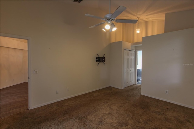 unfurnished room featuring ceiling fan, a towering ceiling, and dark colored carpet