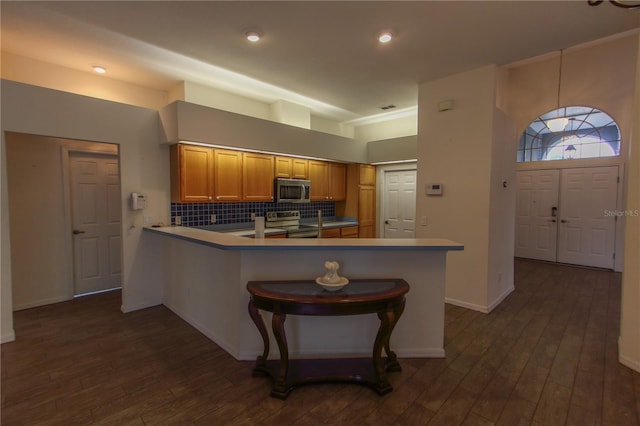 kitchen with kitchen peninsula, dark wood-type flooring, appliances with stainless steel finishes, and tasteful backsplash