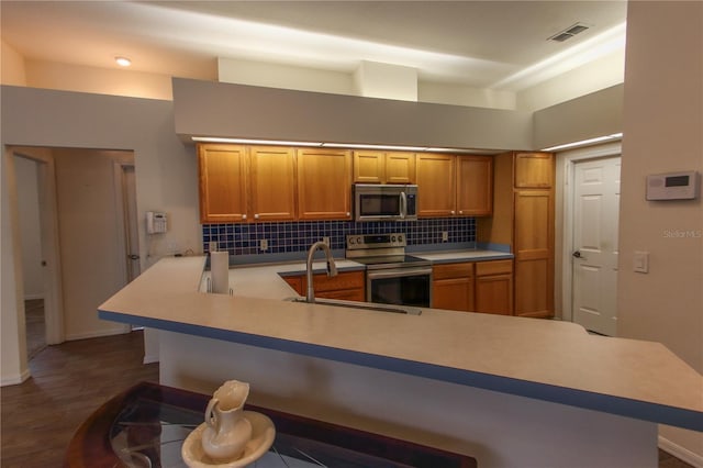 kitchen featuring sink, stainless steel appliances, dark hardwood / wood-style flooring, kitchen peninsula, and decorative backsplash