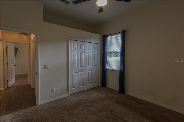 unfurnished bedroom with ceiling fan, dark carpet, and a closet