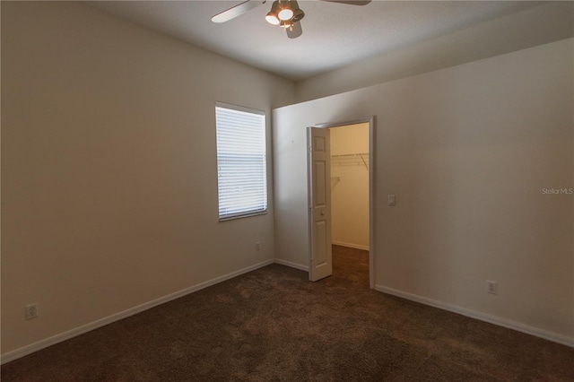 unfurnished bedroom featuring dark carpet, a closet, a spacious closet, and ceiling fan