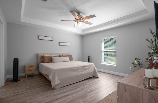 bedroom featuring hardwood / wood-style floors, a raised ceiling, ceiling fan, and ornamental molding