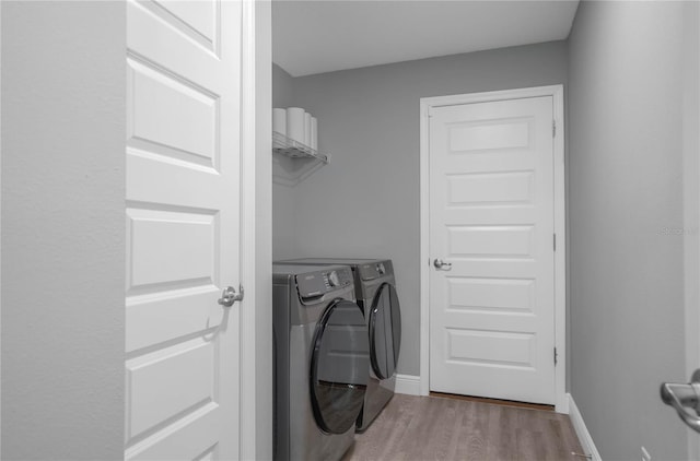 clothes washing area with washing machine and dryer and light wood-type flooring